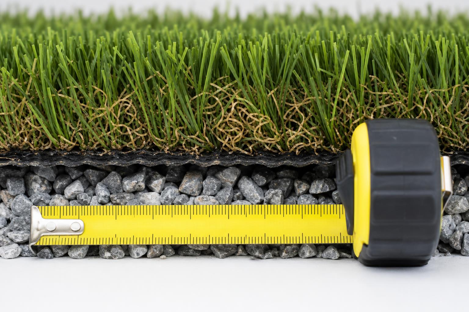 Artificial turf cross-section with measuring tape showing blades, thatch, and crushed-stone base